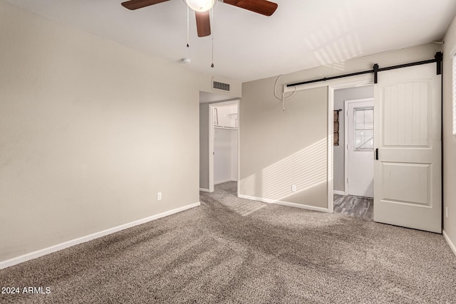 unfurnished bedroom featuring ceiling fan, a barn door, carpet floors, a spacious closet, and a closet