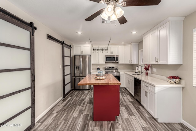 kitchen featuring butcher block counters, appliances with stainless steel finishes, white cabinetry, a barn door, and sink