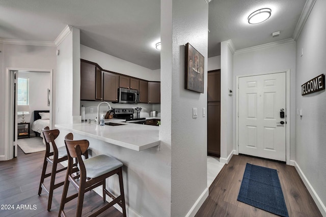 kitchen with dark brown cabinetry, a kitchen bar, dark hardwood / wood-style floors, kitchen peninsula, and stainless steel appliances