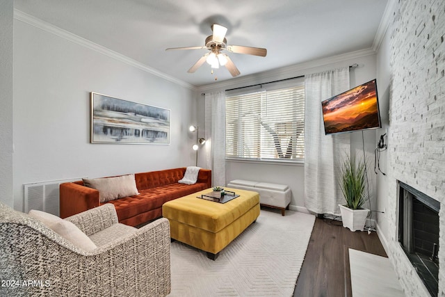 living room with crown molding, a stone fireplace, wood-type flooring, and ceiling fan