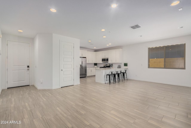 kitchen with a breakfast bar area, stainless steel appliances, white cabinetry, open floor plan, and light countertops