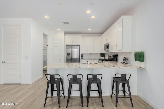 kitchen with a peninsula, appliances with stainless steel finishes, white cabinets, and a sink