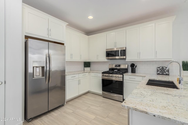 kitchen featuring tasteful backsplash, appliances with stainless steel finishes, light stone counters, white cabinetry, and a sink