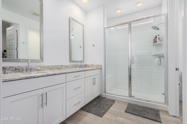 bathroom with double vanity, wood finished floors, a sink, and a shower stall