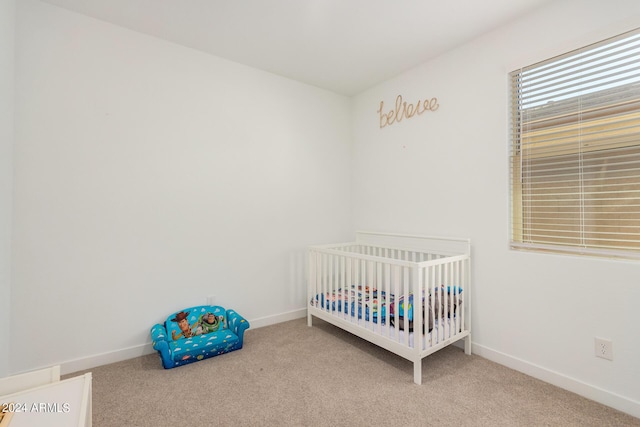 carpeted bedroom featuring a crib and baseboards