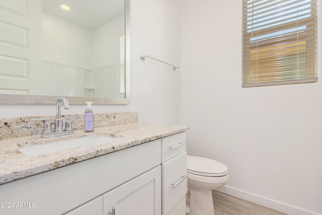 bathroom with toilet, wood finished floors, vanity, and baseboards