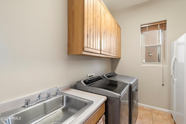 clothes washing area featuring light tile patterned floors, sink, washing machine and clothes dryer, and cabinets