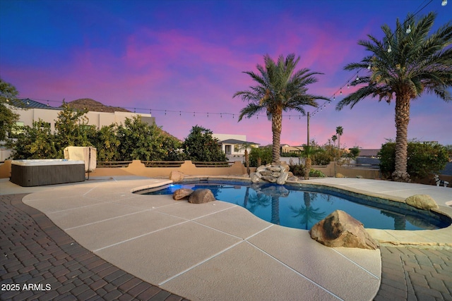 pool at dusk with a patio area and a hot tub