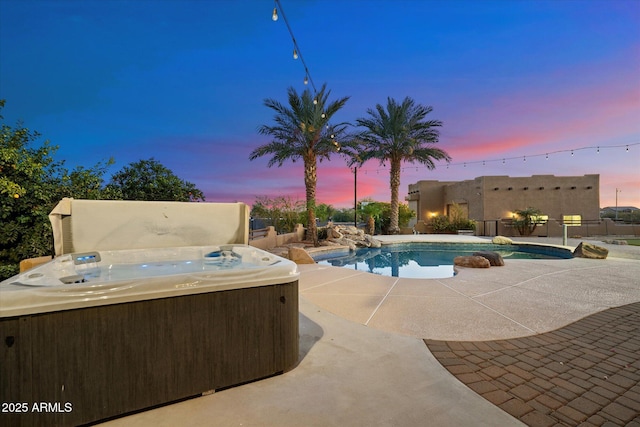 pool at dusk featuring a hot tub and a patio