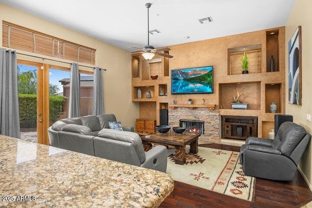 living room with ceiling fan, dark hardwood / wood-style flooring, a fireplace, and built in shelves