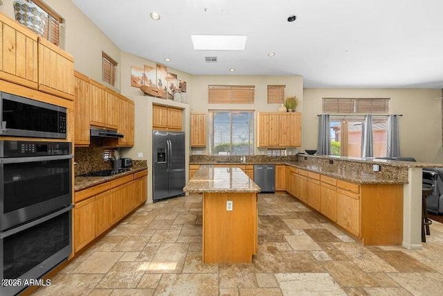 kitchen featuring a center island, a skylight, light stone countertops, a breakfast bar area, and stainless steel appliances