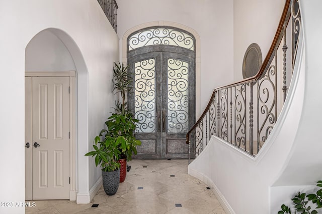foyer entrance with french doors, arched walkways, a high ceiling, stairway, and baseboards
