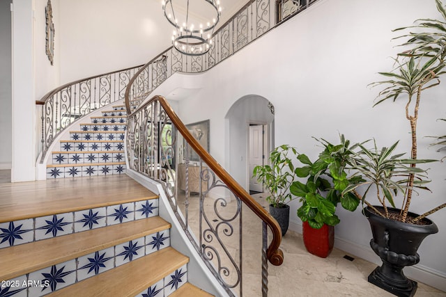 staircase with arched walkways, a chandelier, a towering ceiling, and baseboards