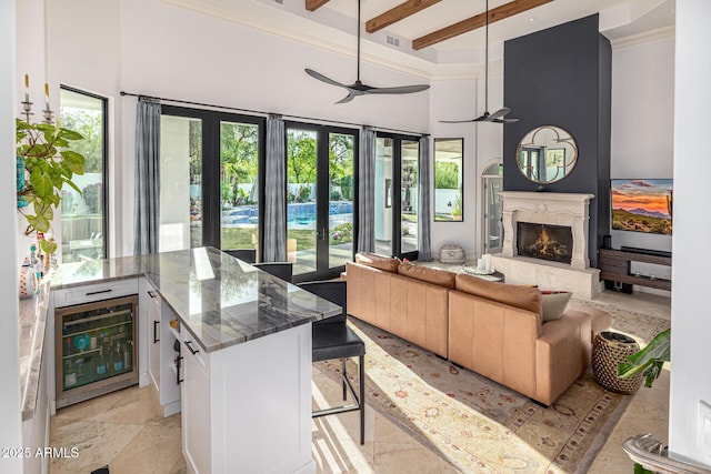 living room with healthy amount of natural light, beverage cooler, a high ceiling, a high end fireplace, and beam ceiling