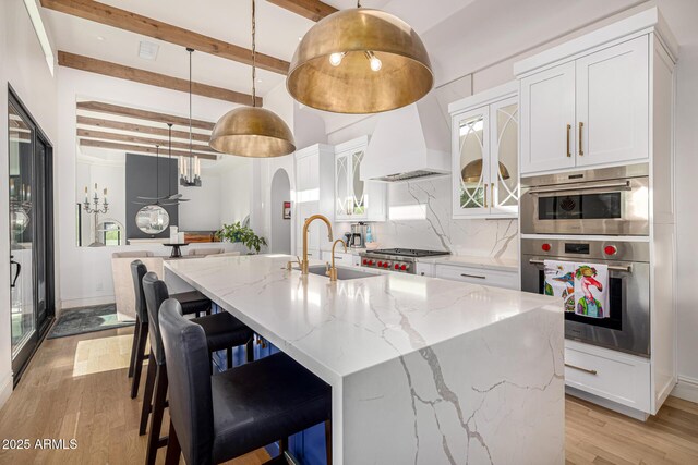 kitchen featuring a sink, tasteful backsplash, beamed ceiling, light wood finished floors, and white cabinets