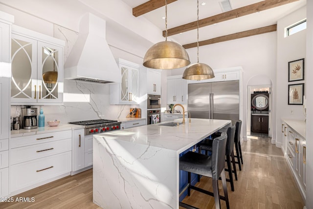 kitchen with custom exhaust hood, a sink, stainless steel appliances, decorative backsplash, and beamed ceiling