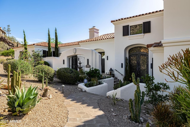 view of front facade featuring a chimney, a tile roof, and stucco siding
