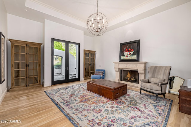 living area with a chandelier, french doors, crown molding, wood finished floors, and a lit fireplace