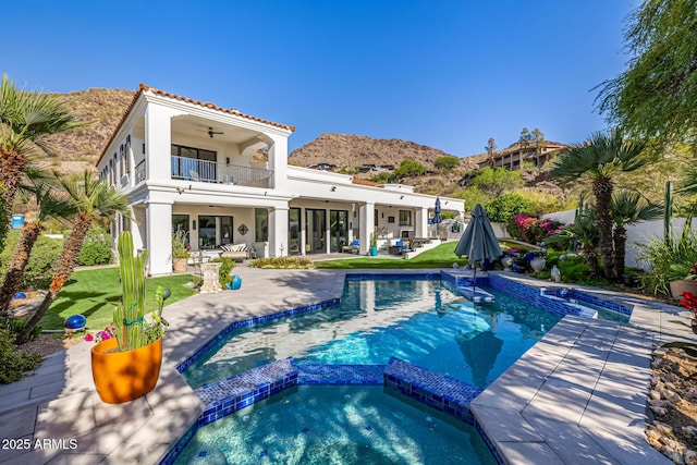 back of house featuring a balcony, a pool with connected hot tub, ceiling fan, a patio area, and a mountain view