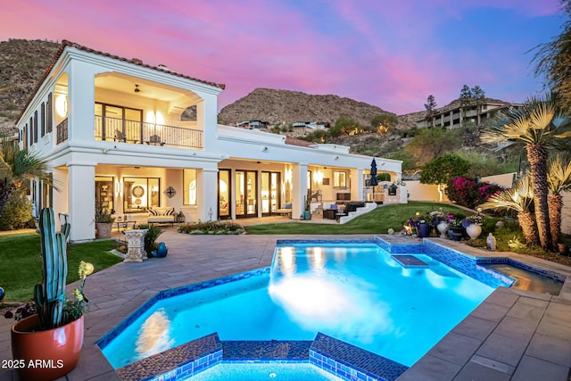 back of property at dusk featuring outdoor lounge area, a balcony, a patio, a lawn, and stucco siding