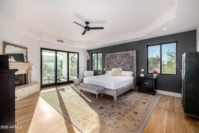 bedroom with a raised ceiling, access to outside, crown molding, light wood-type flooring, and a premium fireplace