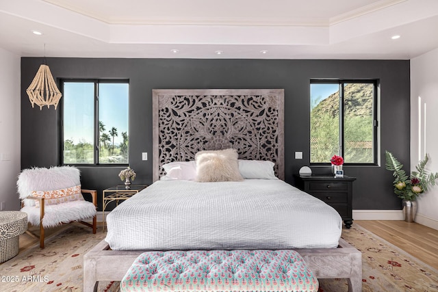 bedroom with a raised ceiling, wood finished floors, multiple windows, crown molding, and recessed lighting