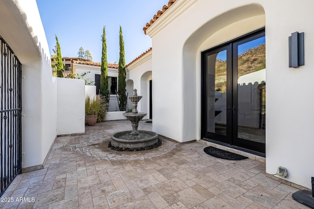 property entrance with french doors, a tile roof, a patio, and stucco siding