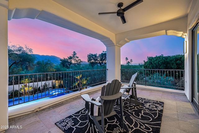 patio terrace at dusk featuring ceiling fan and a balcony