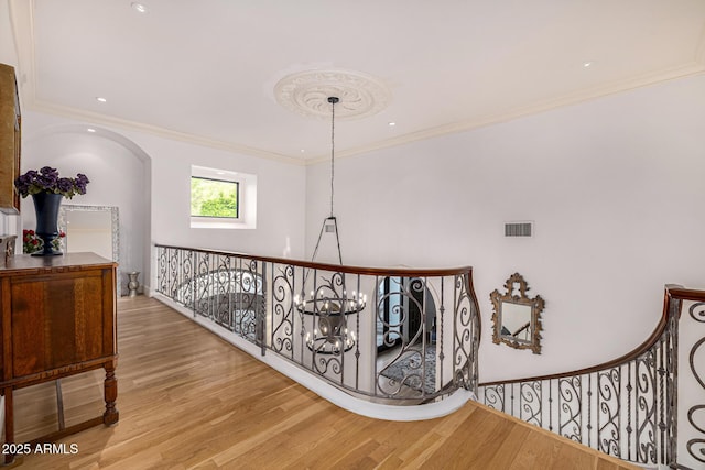 hall with wood finished floors, ornamental molding, and an upstairs landing