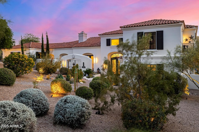 back of house at dusk with a chimney, a tiled roof, and stucco siding