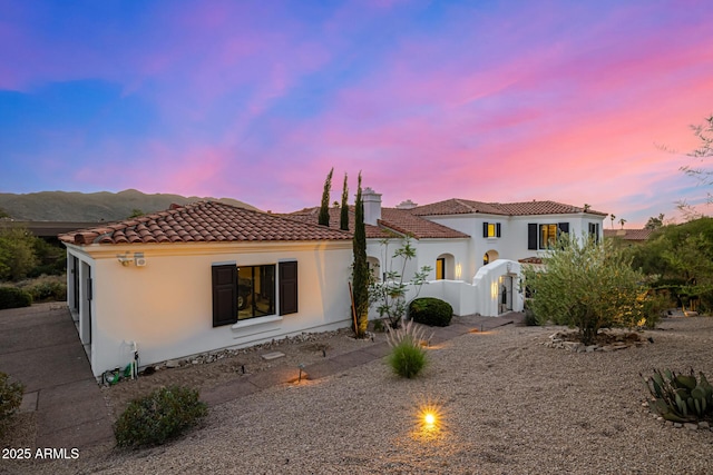 back of property with a tiled roof, a chimney, and stucco siding