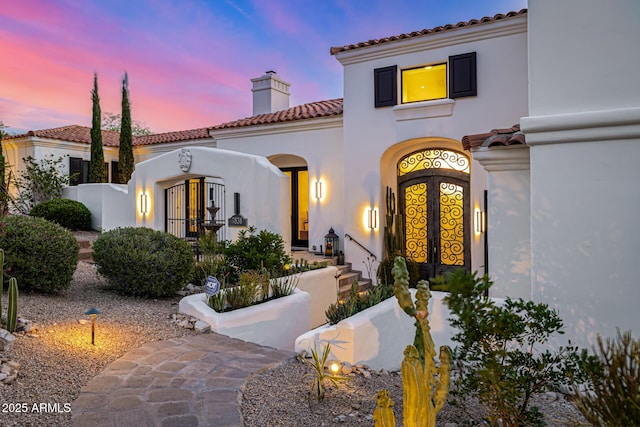 property entrance with a chimney, a tiled roof, and stucco siding