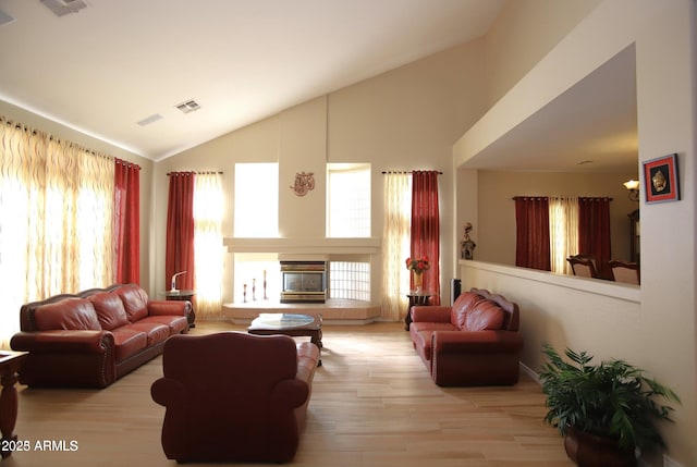 living room featuring a glass covered fireplace, high vaulted ceiling, visible vents, and wood finished floors