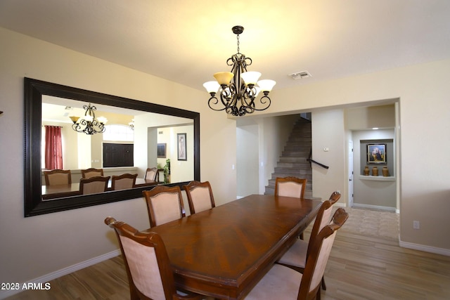 dining room featuring visible vents, a notable chandelier, wood finished floors, and stairs