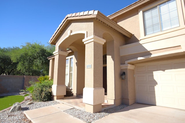 view of exterior entry featuring fence, a garage, and stucco siding