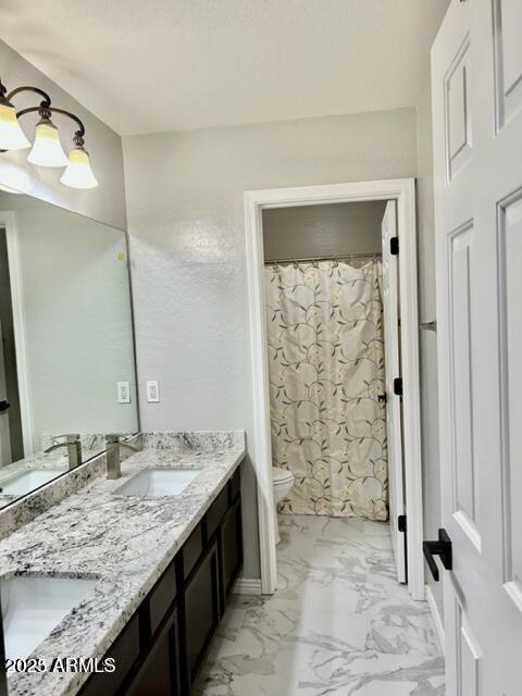bathroom featuring double vanity, marble finish floor, a sink, and toilet