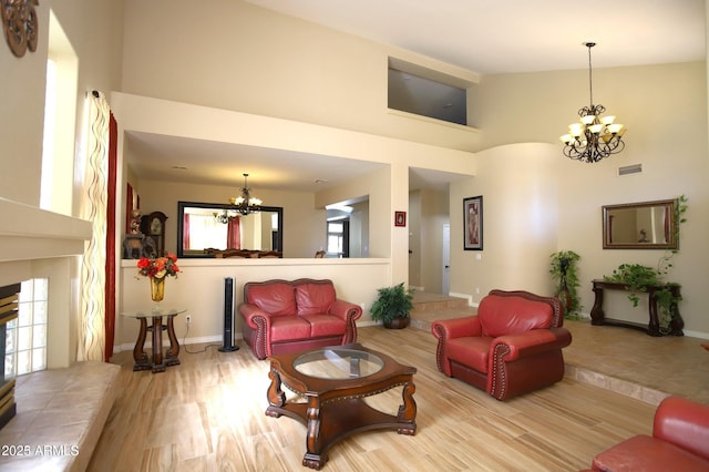 living area with a high ceiling, an inviting chandelier, visible vents, and wood finished floors