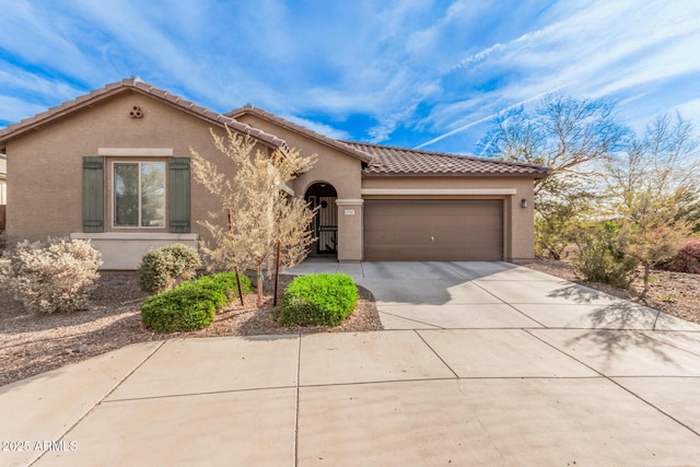 mediterranean / spanish house featuring concrete driveway, an attached garage, a tiled roof, and stucco siding