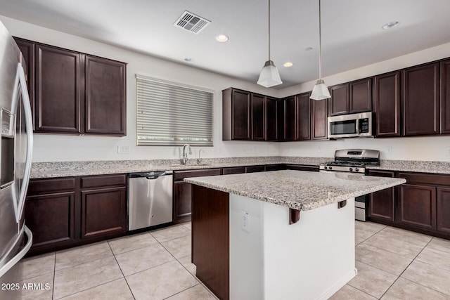 kitchen featuring appliances with stainless steel finishes, light tile patterned floors, a sink, a center island, and dark brown cabinets
