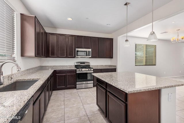 kitchen featuring appliances with stainless steel finishes, a sink, light stone countertops, a kitchen island, and recessed lighting