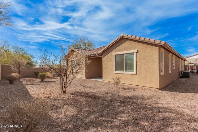 view of side of home featuring cooling unit, a fenced backyard, stucco siding, and a tile roof