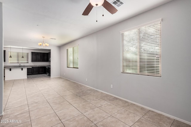 unfurnished living room with a chandelier, ceiling fan, light tile patterned flooring, and baseboards