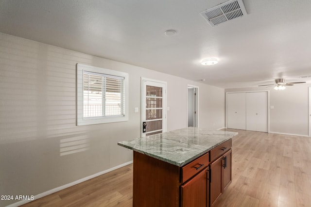 kitchen featuring light hardwood / wood-style flooring, ceiling fan, a kitchen island, and light stone countertops