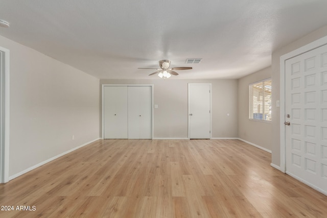 unfurnished bedroom with ceiling fan, a textured ceiling, two closets, and light hardwood / wood-style floors