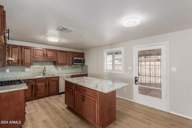 kitchen featuring light wood-type flooring, light stone counters, a center island, sink, and appliances with stainless steel finishes