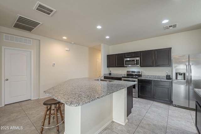 kitchen featuring sink, appliances with stainless steel finishes, a kitchen island with sink, a kitchen breakfast bar, and light stone counters