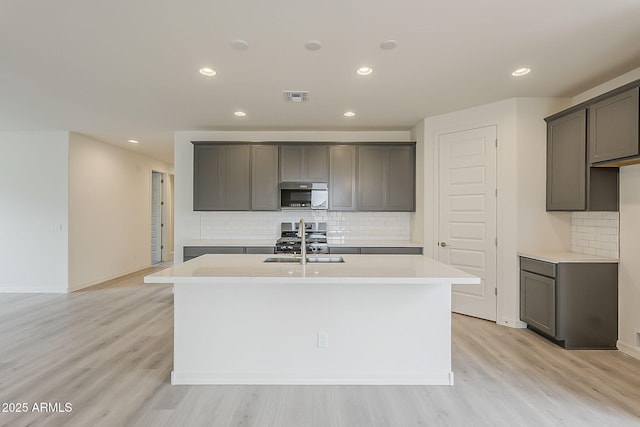 40030 W Bunker Dr, Maricopa, AZ 85138 - kitchen with stainless steel microwave, backsplash, a kitchen island with sink, light wood-style floors, and visible vents