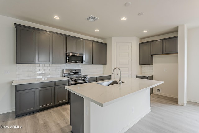40030 W Bunker Dr, Maricopa, AZ 85138 - kitchen with visible vents, a sink, appliances with stainless steel finishes, light wood finished floors, and a center island with sink
