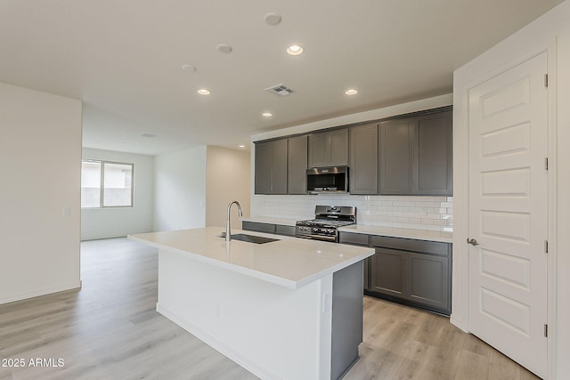 40030 W Bunker Dr, Maricopa, AZ 85138 - kitchen with backsplash, a center island with sink, appliances with stainless steel finishes, light wood finished floors, and a sink