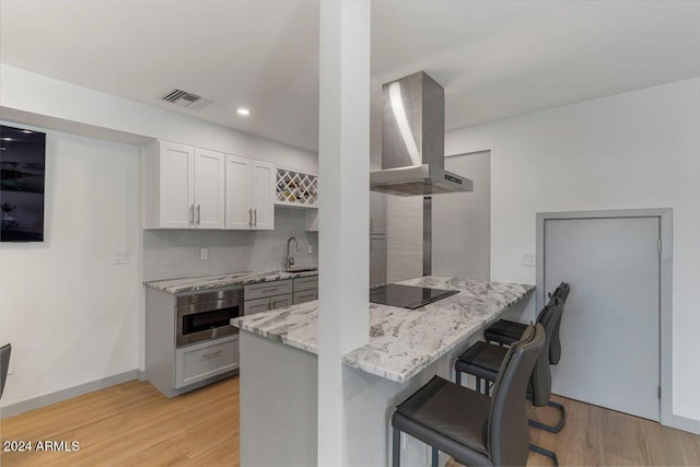 kitchen with decorative backsplash, kitchen peninsula, light wood-type flooring, a breakfast bar area, and range hood